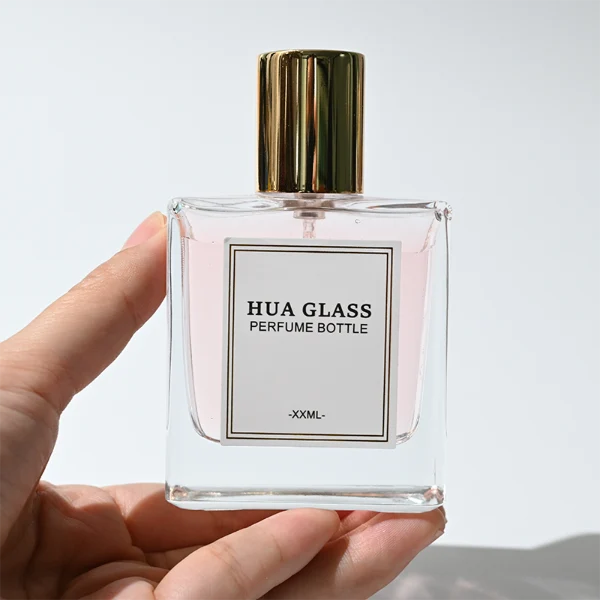 HUA0316 perfume bottle, square transparent colorless glass body with thick base and sharp edges, 30 ml, 50 ml, or 100 ml liquid, straight cylindrical Zinc Alloy cap or cylindrical cap with glossy gold bottle neck, printed label attached on bottle surface, modern minimalist luxury design, ideal for gifting and daily use.