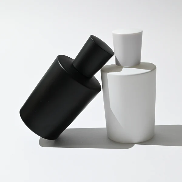 HUA0317 perfume bottle, cylindrical matte black, matte white, or transparent colorless glass body with thick rounded base, 50 ml or 70 ml liquid, flared cylindrical plastic cap in black, white, or gold finish, printed logo or brand label on bottle surface, modern minimalist fashion design, ideal for gifting and daily use.