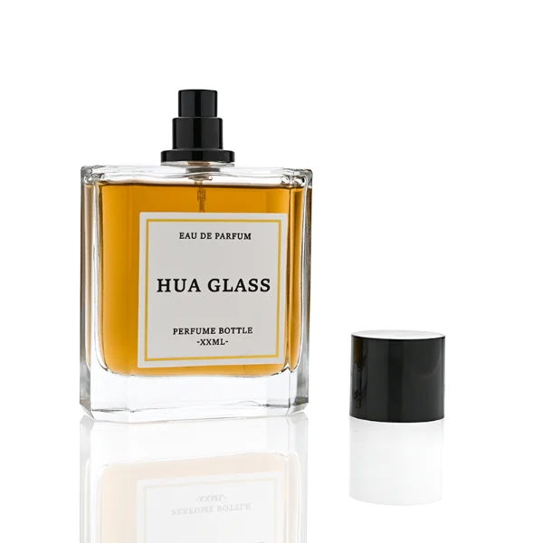 HUA0320 perfume bottle, square transparent colorless glass body with thick base and sharp edges, 50 ml or 100 ml liquid, straight cylindrical Zamac cap in glossy gold or black finish with matching bottle neck, printed label attached on bottle surface, modern minimalist luxury design, ideal for gifting and daily use.