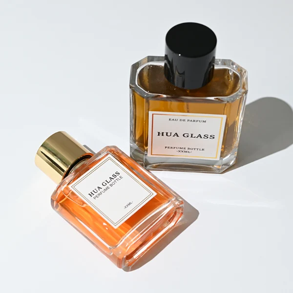HUA0320 perfume bottle, square transparent colorless glass body with thick base and sharp edges, 50 ml or 100 ml liquid, straight cylindrical Zamac cap in glossy gold or black finish with matching bottle neck, printed label attached on bottle surface, modern minimalist luxury design, ideal for gifting and daily use.