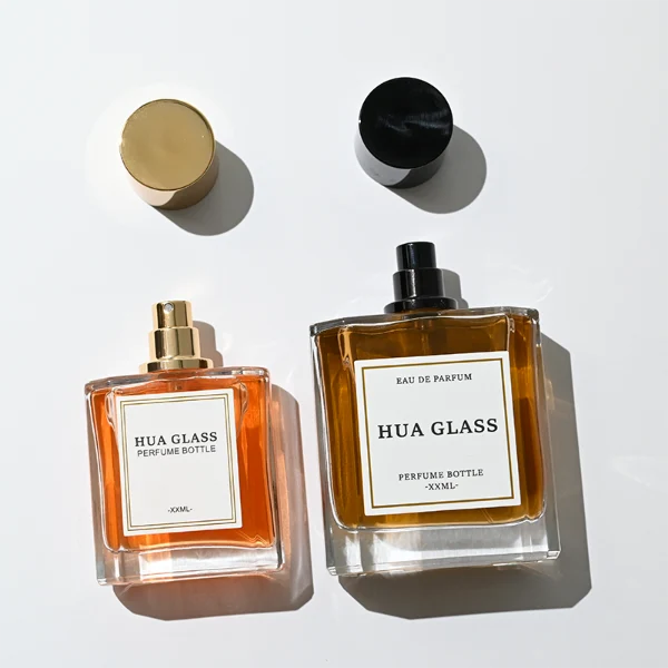 HUA0320 perfume bottle, square transparent colorless glass body with thick base and sharp edges, 50 ml or 100 ml liquid, straight cylindrical Zamac cap in glossy gold or black finish with matching bottle neck, printed label attached on bottle surface, modern minimalist luxury design, ideal for gifting and daily use.