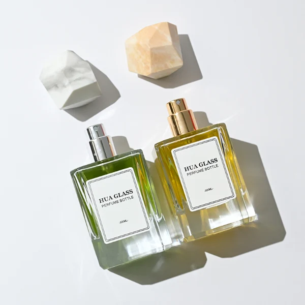 HUA0322 perfume bottle, square transparent colorless glass body with thick base and sharp edges, 30 ml, 50 ml, or 100 ml liquid, irregular geometric stone-inspired plastic cap in beige or marble white color with gold or silver bottle neck, printed label attached on bottle surface, artistic modern luxury design, ideal for gifting and daily use.