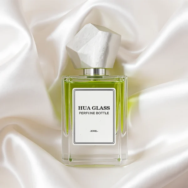HUA0322 perfume bottle, square transparent colorless glass body with thick base and sharp edges, 30 ml, 50 ml, or 100 ml liquid, irregular geometric stone-inspired plastic cap in beige or marble white color with gold or silver bottle neck, printed label attached on bottle surface, artistic modern luxury design, ideal for gifting and daily use.