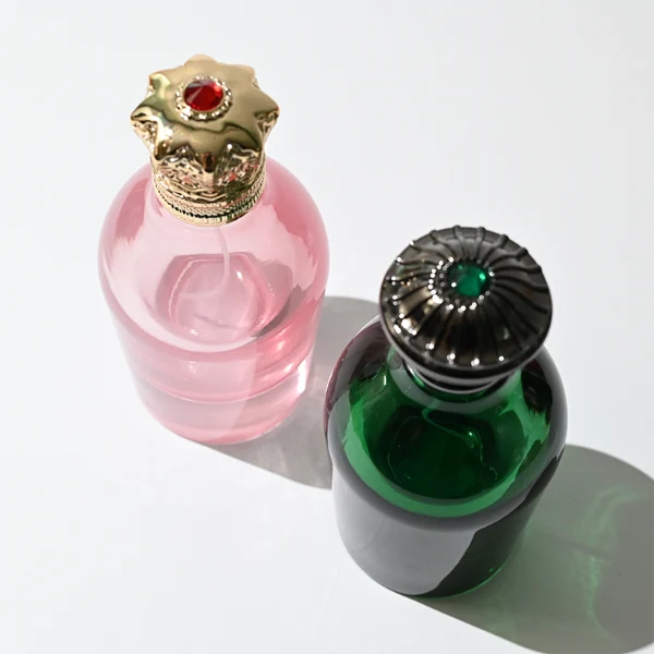 HUA0324 perfume bottle, rounded cylindrical semi-transparent red, blue, or smoky black glass body with thick base, 100 ml liquid, decorative Zamac cap with carved crown-inspired or layered dome design, metallic gold printed logo on bottle surface, vintage luxury artistic style, ideal for gifting and display.