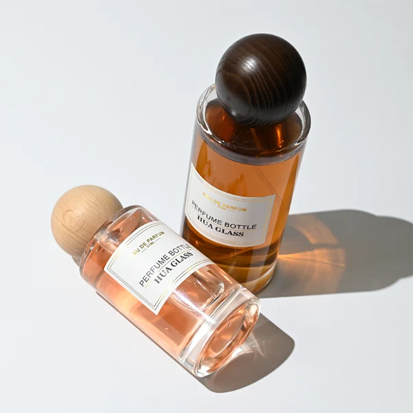 HUA0325 perfume bottle, cylindrical transparent colorless glass body with thick rounded base and smooth silhouette, 30 ml, 50 ml, 100 ml, 200 ml, or 250 ml liquid, spherical wooden cap with natural wood grain texture in light or dark finish, printed label attached on bottle surface, natural modern minimalist design, ideal for gifting and display.