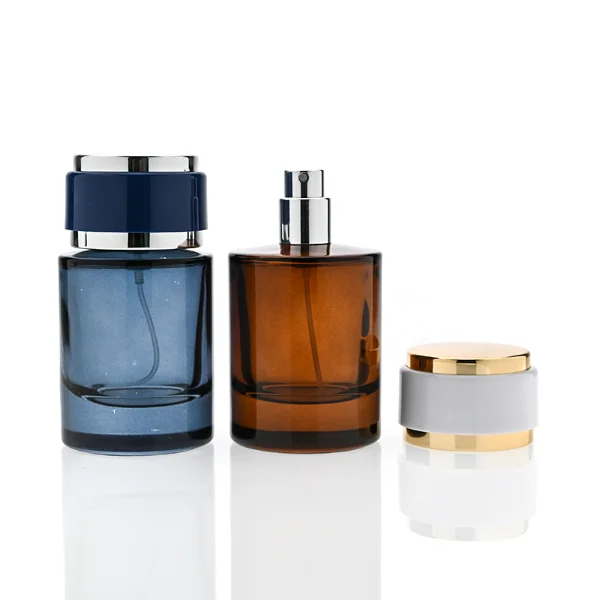 HUA0326 perfume bottle, rounded cylindrical semi-transparent smoky black, amber brown, or blue glass body with thick base, 30 ml, 50 ml, or 100 ml liquid, layered cylindrical plastic cap with black, white, or blue center section and glossy gold or silver accents on both ends, optional metallic gold printed logo or blank bottle surface, modern minimalist luxury design, ideal for gifting and daily use.
