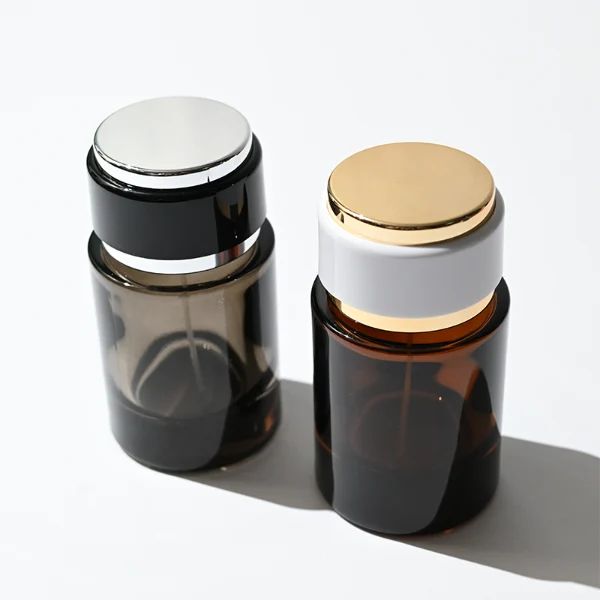 HUA0326 perfume bottle, rounded cylindrical semi-transparent smoky black, amber brown, or blue glass body with thick base, 30 ml, 50 ml, or 100 ml liquid, layered cylindrical plastic cap with black, white, or blue center section and glossy gold or silver accents on both ends, optional metallic gold printed logo or blank bottle surface, modern minimalist luxury design, ideal for gifting and daily use.