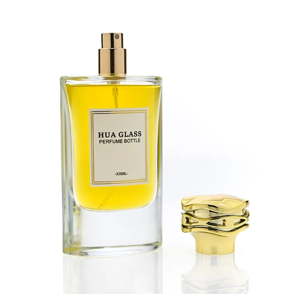 HUA0327 perfume bottle, minimalist geometric cylindrical transparent glass body with smooth curved sides and thick base, 80 ml liquid, irregular geometric plastic cap with side wave-texture in glossy gold or silver finish, printed label on bottle surface, modern minimalist luxury design, ideal for gifting and daily use.