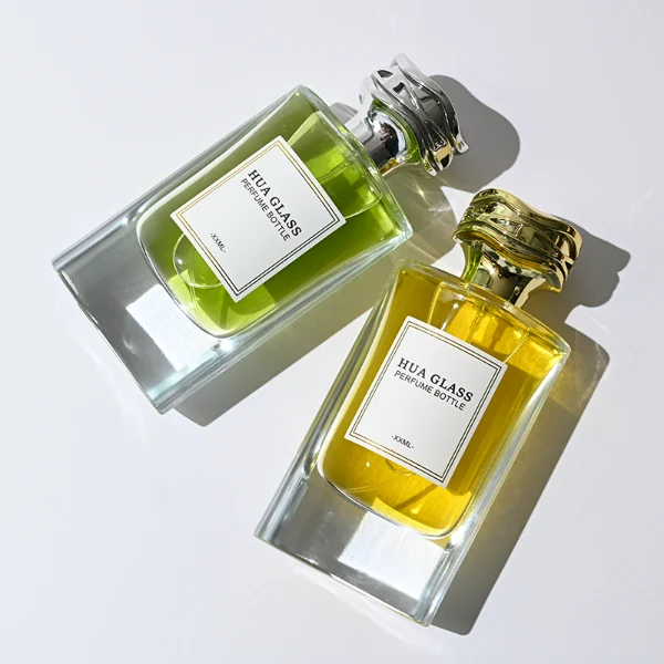 HUA0327 perfume bottle, minimalist geometric cylindrical transparent glass body with smooth curved sides and thick base, 80 ml liquid, irregular geometric plastic cap with side wave-texture in glossy gold or silver finish, printed label on bottle surface, modern minimalist luxury design, ideal for gifting and daily use.