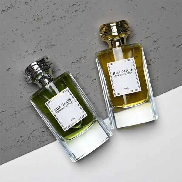 HUA0327 perfume bottle, minimalist geometric cylindrical transparent glass body with smooth curved sides and thick base, 80 ml liquid, irregular geometric plastic cap with side wave-texture in glossy gold or silver finish, printed label on bottle surface, modern minimalist luxury design, ideal for gifting and daily use.