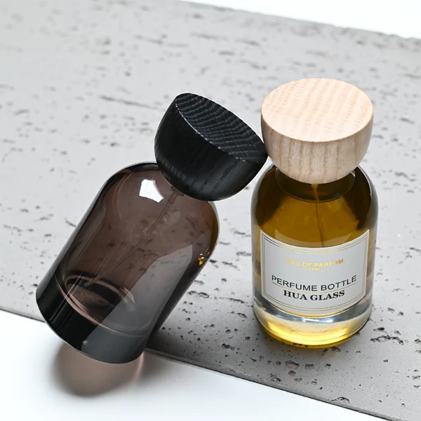 HUA0331 perfume bottle, rounded cylindrical transparent or semi-transparent smoky brown glass body with thick base, 30 ml, 50 ml, or 100 ml liquid, semi-spherical wooden cap in natural wood or black color, gold bottle neck, printed label or blank bottle surface, modern natural luxury design, ideal for gifting and daily use.