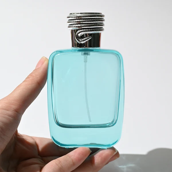 HUA0337 perfume bottle, rounded rectangular transparent colorless glass body with light blue tint, 50 ml or 100 ml liquid, silver cylindrical plastic cap with rope-inspired decorative detail, silver bottle neck, gold printed brand logo on bottle surface, modern minimalist luxury design, ideal for gifting and daily use.