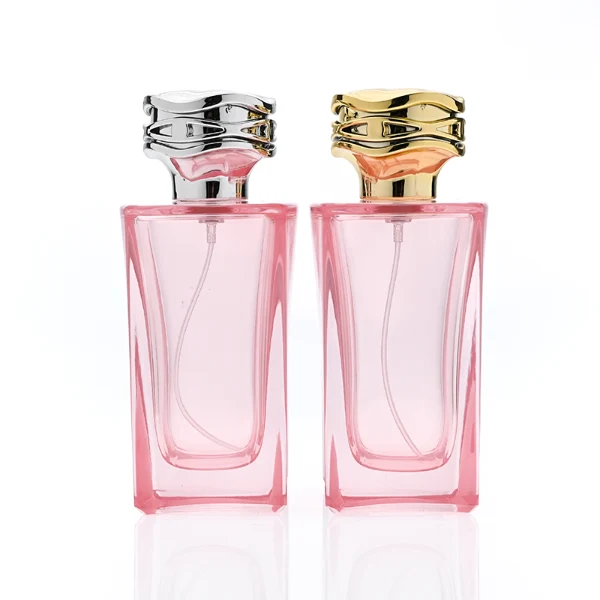 HUA0338 perfume bottle, rectangular transparent pink glass body with curved inner contour and thick base, 100 ml liquid, irregular geometric plastic cap with wave-pattern side texture in gold or silver finish, matching metallic bottle neck, clean bottle surface for logo printing or label application, elegant feminine luxury design, ideal for gifting and daily use.