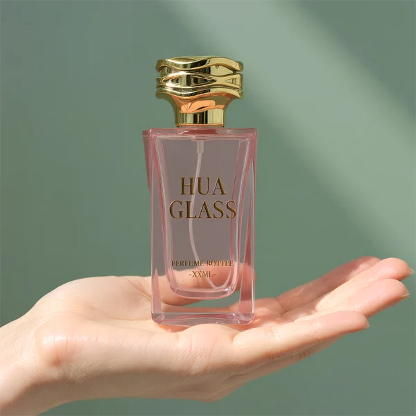 HUA0338 perfume bottle, rectangular transparent pink glass body with curved inner contour and thick base, 100 ml liquid, irregular geometric plastic cap with wave-pattern side texture in gold or silver finish, matching metallic bottle neck, clean bottle surface for logo printing or label application, elegant feminine luxury design, ideal for gifting and daily use.