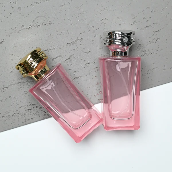 HUA0338 perfume bottle, rectangular transparent pink glass body with curved inner contour and thick base, 100 ml liquid, irregular geometric plastic cap with wave-pattern side texture in gold or silver finish, matching metallic bottle neck, clean bottle surface for logo printing or label application, elegant feminine luxury design, ideal for gifting and daily use.