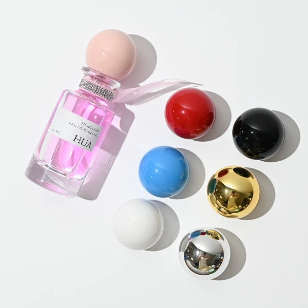 HUA0063 perfume bottle, heavy-base slender cylindrical round glass bottle with clear finish, featuring a square paper label, a matching neck with ribbon bow decorations, and a playful spherical ball-shaped plastic cap with a smooth high-gloss shiny finish, elegant modern fragrance packaging design available in 30ml, 50ml, and 100ml