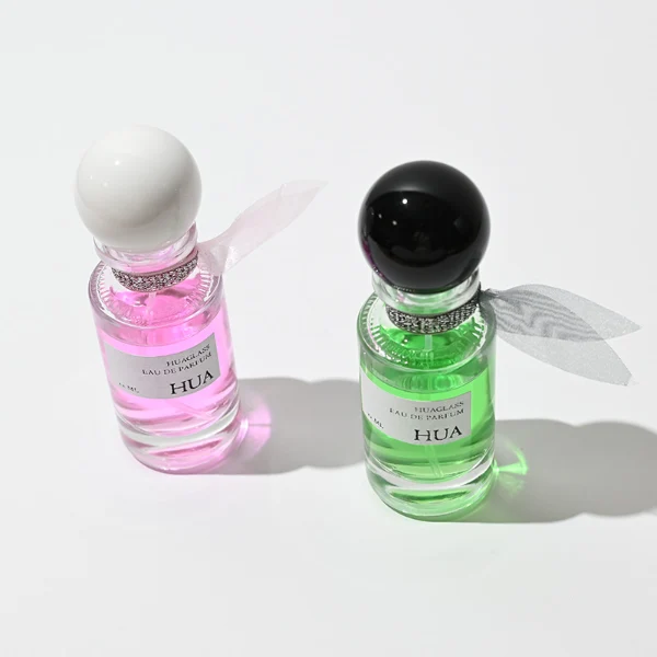 HUA0063 perfume bottle, heavy-base slender cylindrical round glass bottle with clear finish, featuring a square paper label, a matching neck with ribbon bow decorations, and a playful spherical ball-shaped plastic cap with a smooth high-gloss shiny finish, elegant modern fragrance packaging design available in 30ml, 50ml, and 100ml