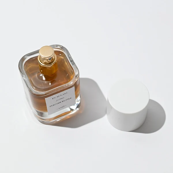 HUA0003 perfume bottles, sleek cylindrical clear glass with glossy black and white caps, golden-amber fragrance, timeless contemporary design, 30ml 50ml 100ml.
