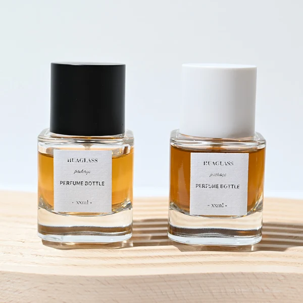 HUA0003 perfume bottles, sleek cylindrical clear glass with glossy black and white caps, golden-amber fragrance, timeless contemporary design, 30ml 50ml 100ml.