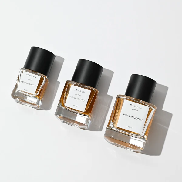 HUA0003 perfume bottles, sleek cylindrical clear glass with glossy black and white caps, golden-amber fragrance, timeless contemporary design, 30ml 50ml 100ml.