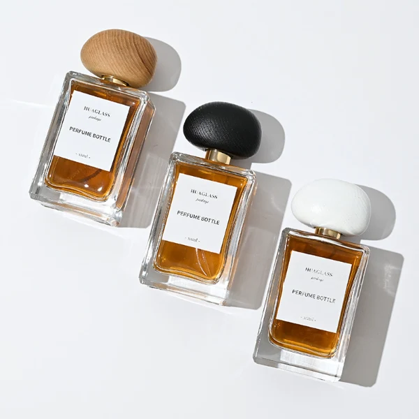 HUA0014 perfume bottle, heavy-base rectangular cuboid glass bottle with clear finish, featuring a square paper label, a polished gold neck, and an organic pebble-shaped timber cap with a natural smooth grain finish, elegant modern fragrance packaging design available in 100ml