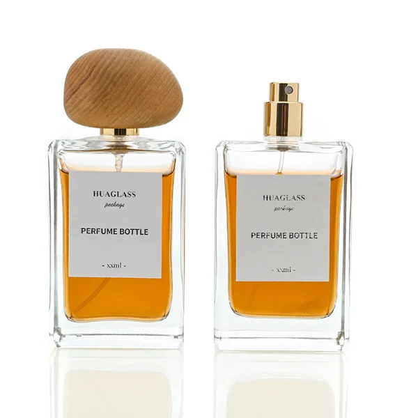 HUA0014 perfume bottle, heavy-base rectangular cuboid glass bottle with clear finish, featuring a square paper label, a polished gold neck, and an organic pebble-shaped timber cap with a natural smooth grain finish, elegant modern fragrance packaging design available in 100ml