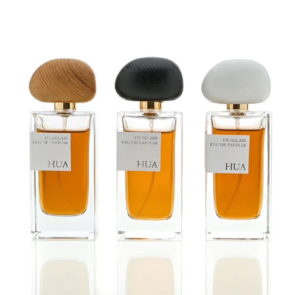 HUA0016 perfume bottle, heavy-base rectangular cuboid glass bottle with clear finish, featuring a square paper label, a polished gold neck, and an organic pebble-shaped timber cap with a natural smooth grain finish, elegant modern fragrance packaging design available in 30ml, 50ml, and 100ml
