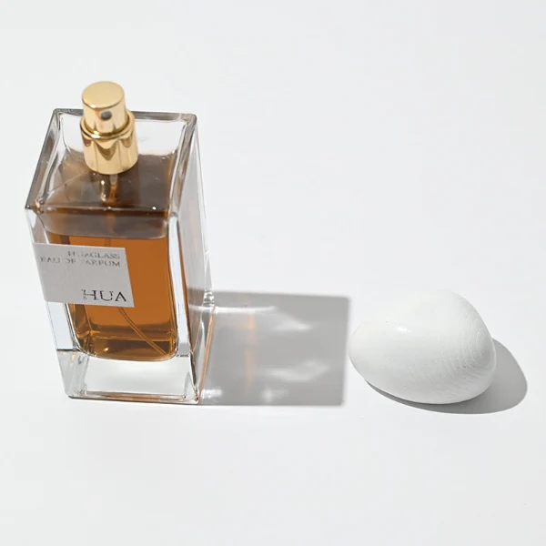 HUA0016 perfume bottle, heavy-base rectangular cuboid glass bottle with clear finish, featuring a square paper label, a polished gold neck, and an organic pebble-shaped timber cap with a natural smooth grain finish, elegant modern fragrance packaging design available in 30ml, 50ml, and 100ml