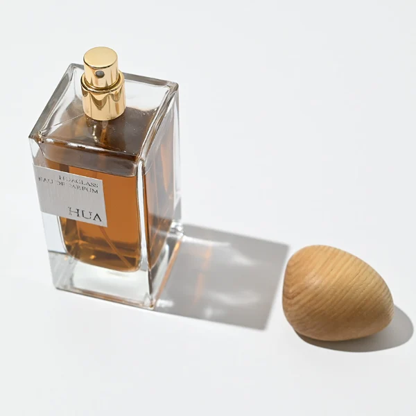 HUA0016 perfume bottle, heavy-base rectangular cuboid glass bottle with clear finish, featuring a square paper label, a polished gold neck, and an organic pebble-shaped timber cap with a natural smooth grain finish, elegant modern fragrance packaging design available in 30ml, 50ml, and 100ml