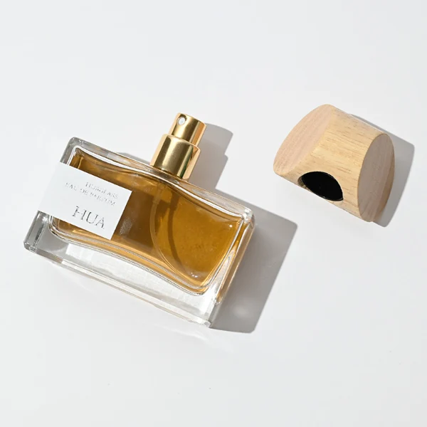 HUA0054 perfume bottle, heavy-base wide rectangular cuboid glass bottle with clear finish, featuring a gold collar neck accent and a unique horizontally oriented cylindrical barrel-shaped wood cap with subtle grain textures in a shiny charcoal black or natural light wood finish, elegant modern fragrance packaging design available in 30ml, 50ml, and 100ml.