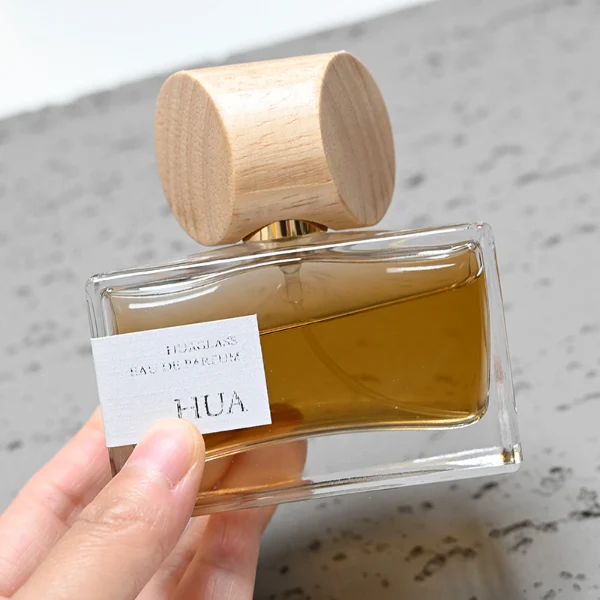 HUA0054 perfume bottle, heavy-base wide rectangular cuboid glass bottle with clear finish, featuring a gold collar neck accent and a unique horizontally oriented cylindrical barrel-shaped wood cap with subtle grain textures in a shiny charcoal black or natural light wood finish, elegant modern fragrance packaging design available in 30ml, 50ml, and 100ml.