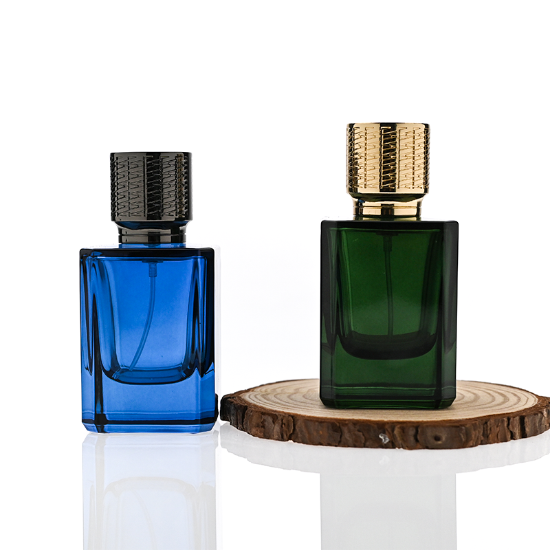 HUA0308 perfume bottle, semi-transparent blue or dark green customizable glass body with thick base and clean rectangular silhouette, 30 ml, 50 ml, or 100 ml liquid, textured cylindrical plastic cap in gold or black finish, gold or white printed logo on bottle surface, modern masculine luxury design, ideal for gifting and daily use.