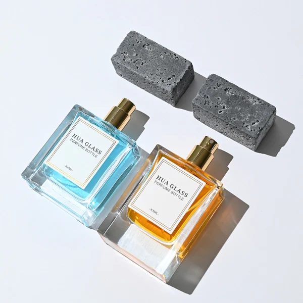 HUA0341 perfume bottle, rectangular transparent colorless glass body with thick base and curved inner contour, 50 ml liquid, oversized rectangular artificial stone cap with matte textured surface, no bottle neck, brand logo label attached on bottle surface, modern architectural luxury design, ideal for gifting and daily use.