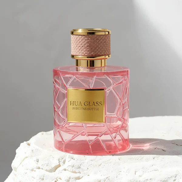 HUA0342 perfume bottle, cylindrical transparent pink glass body with fragmented surface texture, 50 ml or 100 ml liquid, gold plastic cap with textured pink or black side surface and glossy gold top, gold bottle neck, aluminum brand label attached on bottle surface, modern feminine luxury design, ideal for gifting and daily use.