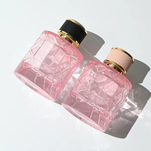 HUA0342 perfume bottle, cylindrical transparent pink glass body with fragmented surface texture, 50 ml or 100 ml liquid, gold plastic cap with textured pink or black side surface and glossy gold top, gold bottle neck, aluminum brand label attached on bottle surface, modern feminine luxury design, ideal for gifting and daily use.