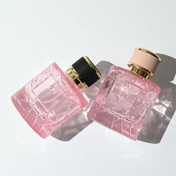 HUA0342 perfume bottle, cylindrical transparent pink glass body with fragmented surface texture, 50 ml or 100 ml liquid, gold plastic cap with textured pink or black side surface and glossy gold top, gold bottle neck, aluminum brand label attached on bottle surface, modern feminine luxury design, ideal for gifting and daily use.