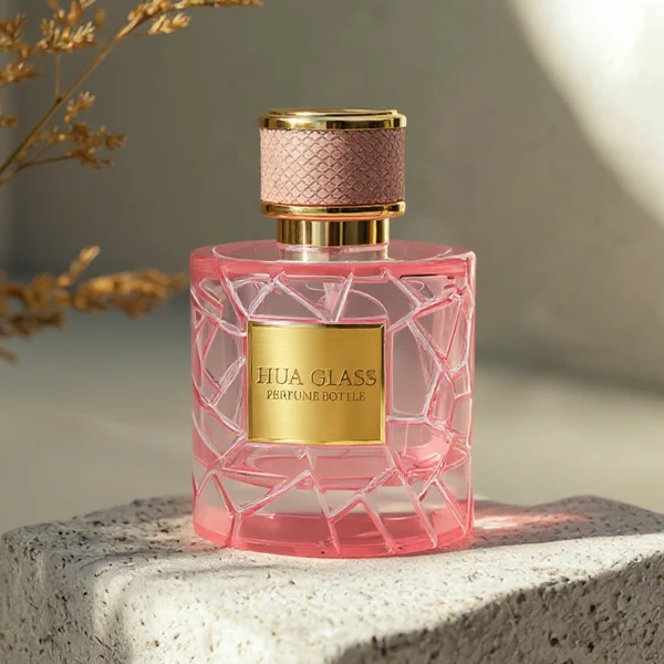 HUA0342 perfume bottle, cylindrical transparent pink glass body with fragmented surface texture, 50 ml or 100 ml liquid, gold plastic cap with textured pink or black side surface and glossy gold top, gold bottle neck, aluminum brand label attached on bottle surface, modern feminine luxury design, ideal for gifting and daily use.