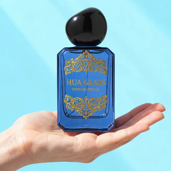 HUA0343 perfume bottle, rectangular semi-transparent blue, pink, amber, or smoky black glass body with beveled edges and thick base, 30 ml, 50 ml, or 100 ml liquid, glossy black spherical plastic cap with smooth polished surface, black bottle neck, gold printed brand logo on bottle surface, modern artistic luxury design, ideal for gifting and daily use.