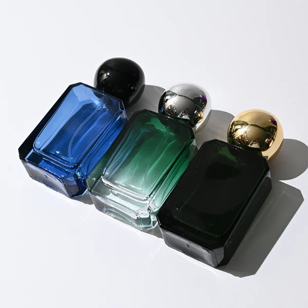 HUA0343 perfume bottle, rectangular semi-transparent blue, pink, amber, or smoky black glass body with beveled edges and thick base, 30 ml, 50 ml, or 100 ml liquid, glossy black spherical plastic cap with smooth polished surface, black bottle neck, gold printed brand logo on bottle surface, modern artistic luxury design, ideal for gifting and daily use.