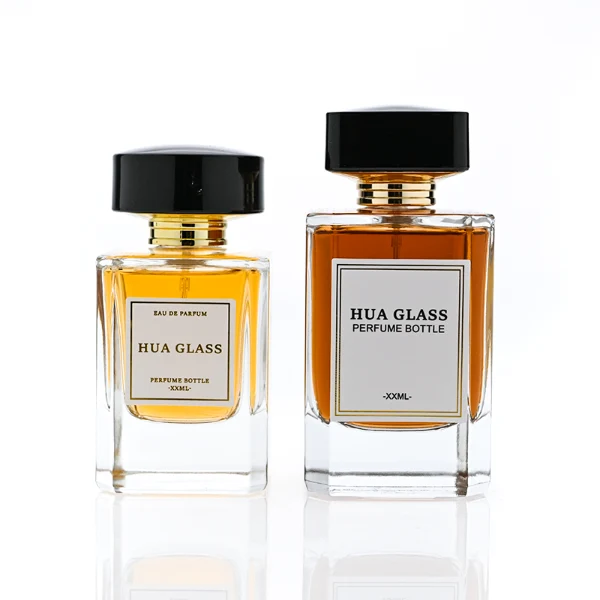 HUA0344 perfume bottle, rectangular transparent colorless glass body with beveled edges and thick base, 30 ml, 50 ml, or 100 ml liquid, wide glossy black cylindrical plastic cap with convex top and flat sides, gold screw-type bottle neck, brand logo label attached on bottle surface, modern minimalist luxury design, ideal for gifting and daily use.