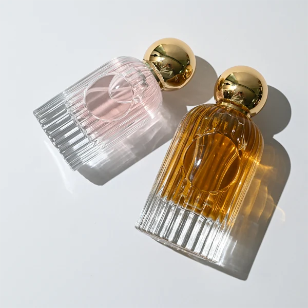 HUA0345 perfume bottle, cylindrical transparent colorless glass body with vertical ribbed texture, 50 ml or 100 ml liquid, spherical glossy gold plastic cap with magnetic closure, gold bottle neck, gold aluminum label attached on bottle surface, elegant luxury design, ideal for gifting and daily use.