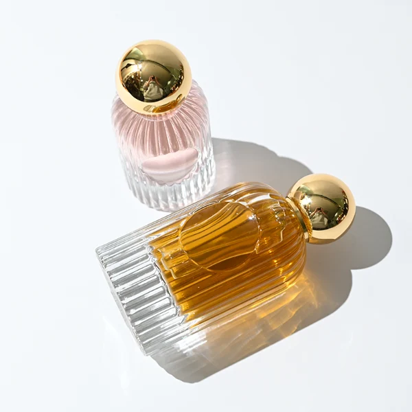 HUA0345 perfume bottle, cylindrical transparent colorless glass body with vertical ribbed texture, 50 ml or 100 ml liquid, spherical glossy gold plastic cap with magnetic closure, gold bottle neck, gold aluminum label attached on bottle surface, elegant luxury design, ideal for gifting and daily use.