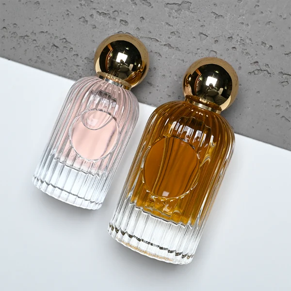 HUA0345 perfume bottle, cylindrical transparent colorless glass body with vertical ribbed texture, 50 ml or 100 ml liquid, spherical glossy gold plastic cap with magnetic closure, gold bottle neck, gold aluminum label attached on bottle surface, elegant luxury design, ideal for gifting and daily use.
