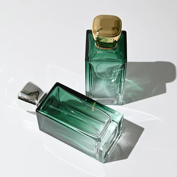 HUA0346 perfume bottle, rectangular transparent colorless glass body with gradient blue, green, or amber tint, 100 ml liquid, glossy square plastic cap with smooth curved sides, no bottle neck, gold printed brand logo on bottle surface, modern luxury minimalist design, ideal for gifting and daily use.
