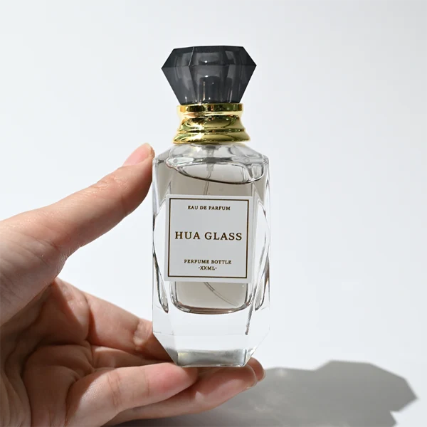 HUA0352 perfume bottle, multi-faceted geometric cut glass body with clear or black diamond-shaped plastic cap and gold collar, minimalist paper label with elegant gold lettering, modern luxury fragrance packaging design