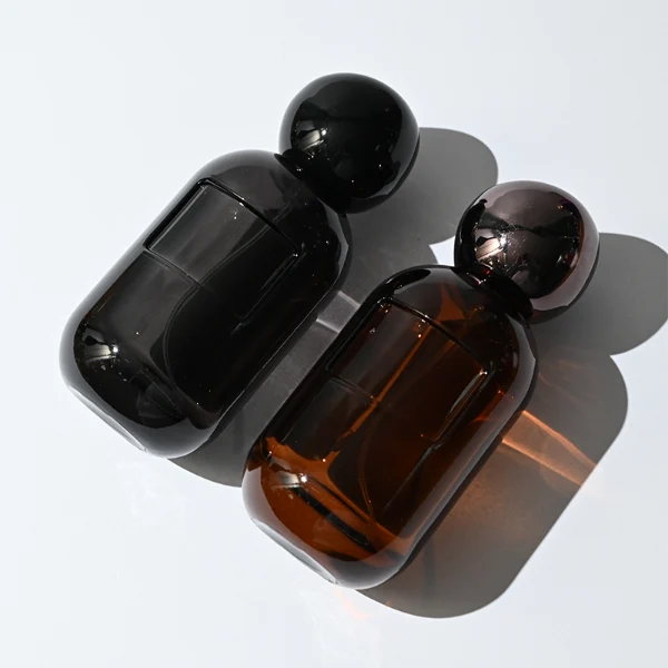 HUA0355 perfume bottle, colored cylindrical glass body in amber brown, purple, and burgundy red with gold aluminum label plate, irregular sculptural pebble plastic cap, luxury artistic vintage fragrance packaging design