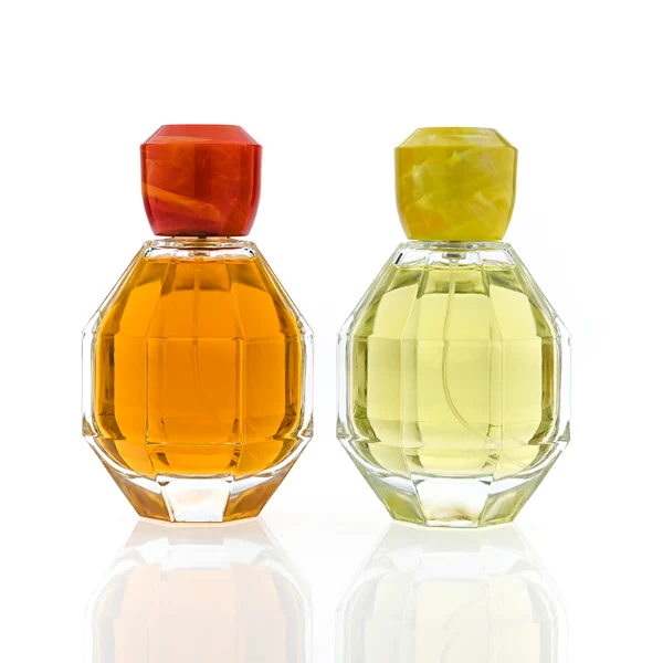 HUA0357 perfume bottle, multi-faceted geometric cut spherical clear glass body with orange-red or yellow marble-textured resin cap, centered square minimalist paper label, contemporary artistic luxury fragrance packaging design
