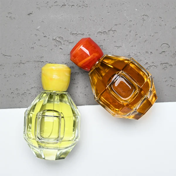 HUA0357 perfume bottle, multi-faceted geometric cut spherical clear glass body with orange-red or yellow marble-textured resin cap, centered square minimalist paper label, contemporary artistic luxury fragrance packaging design