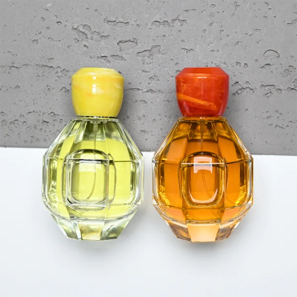 HUA0357 perfume bottle, multi-faceted geometric cut spherical clear glass body with orange-red or yellow marble-textured resin cap, centered square minimalist paper label, contemporary artistic luxury fragrance packaging design