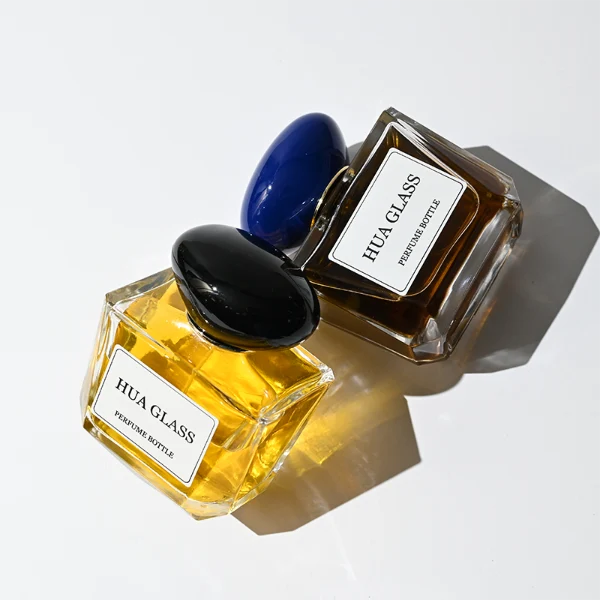 HUA0359 perfume bottle, low rectangular clear glass body with gold neck and a paper label attached, smooth oval pebble plastic cap in navy blue, white, or burgundy, contemporary artistic luxury fragrance packaging design available in 50ml and 100ml